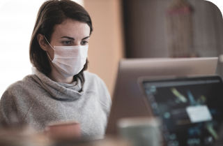 A woman wearing a face mask diligently works on her laptop.